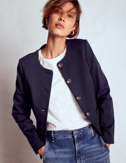 Person wearing a navy blue jacket over a white shirt and blue jeans on a plain background