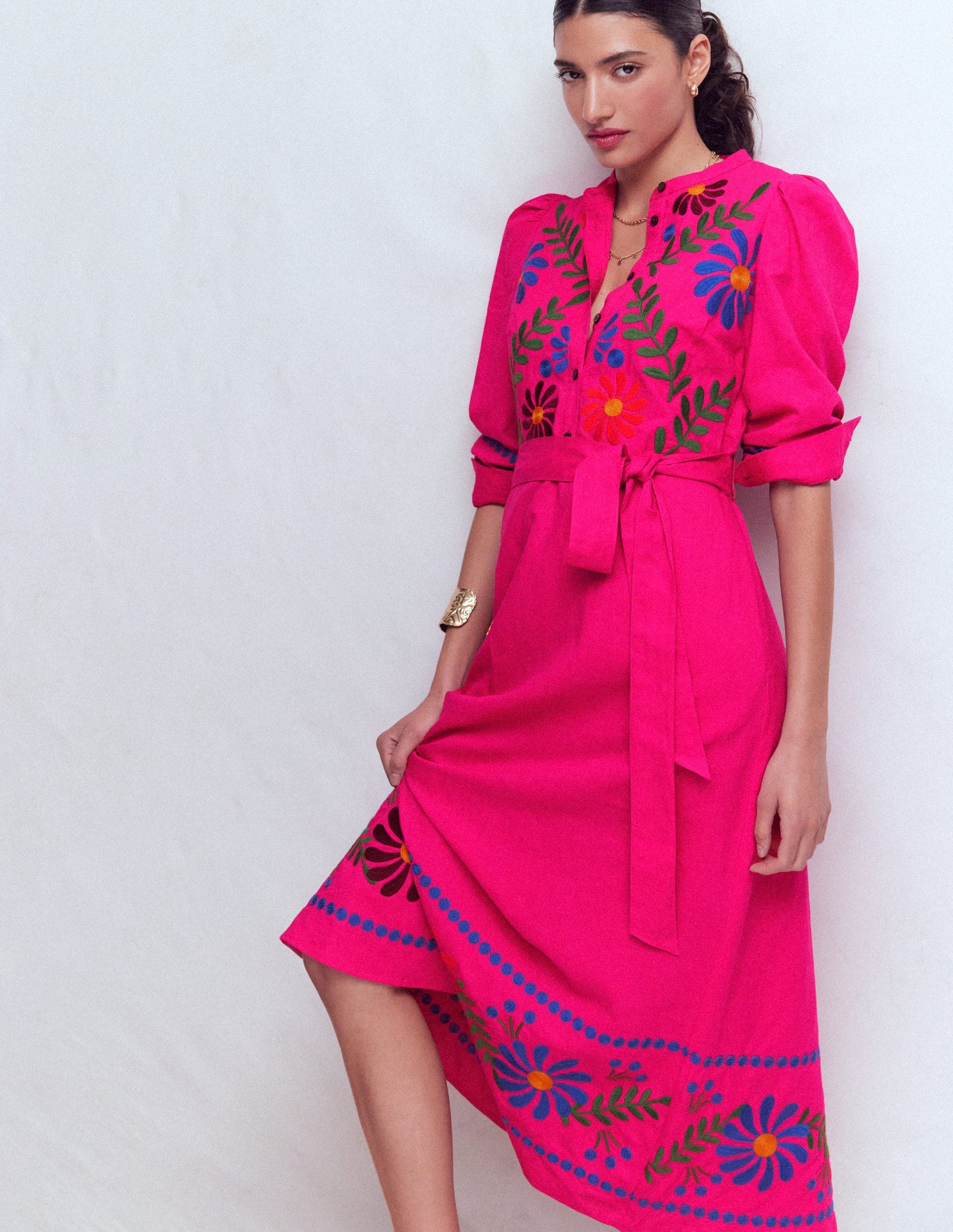 Woman wearing a bright pink dress with colorful floral embroidery on a white background
