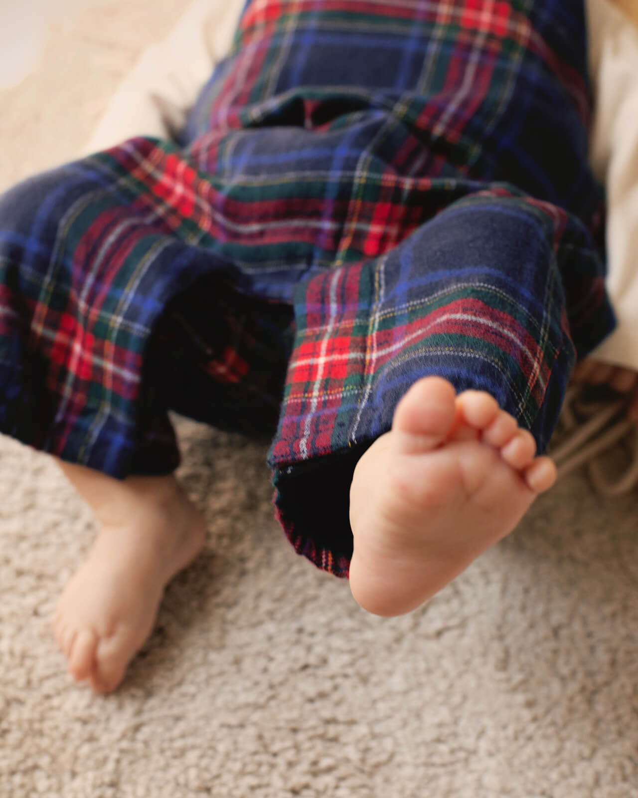 Close-up of a child's feet wearing plaid pants on a carpeted floor.