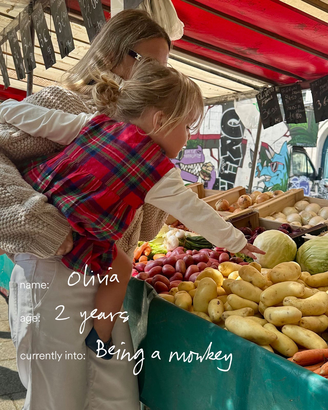 Two women and a child at an outdoor market with produce.