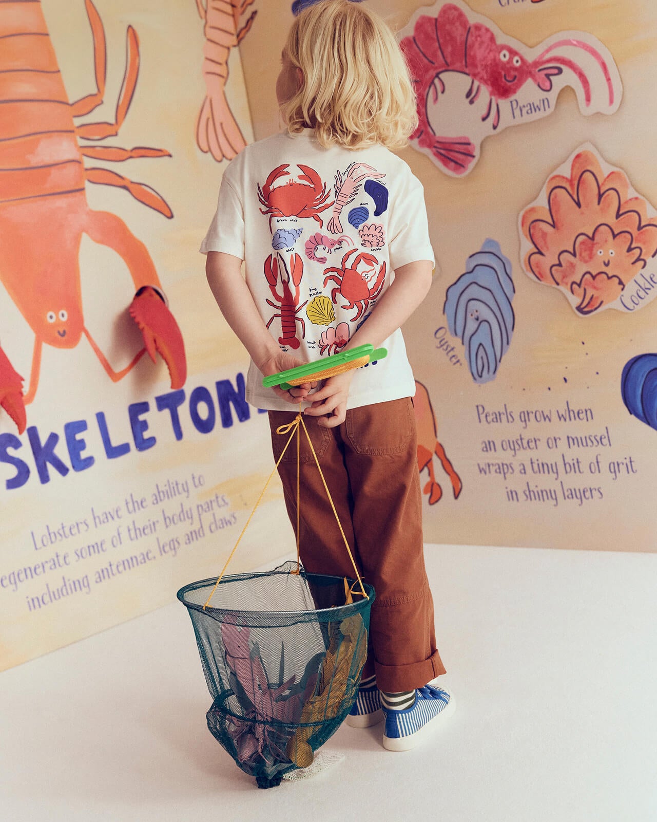 Child holding a fishing net in front of a colorful educational wall chart.