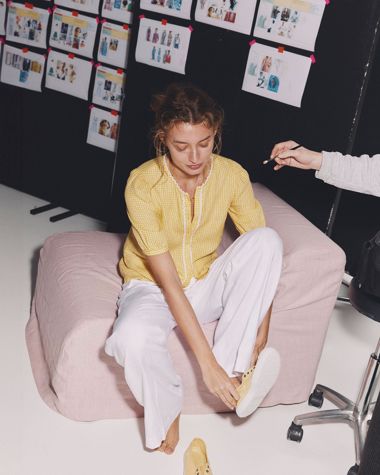 Woman sitting on a pink chair wearing a yellow top and white pants, with another person assisting them.