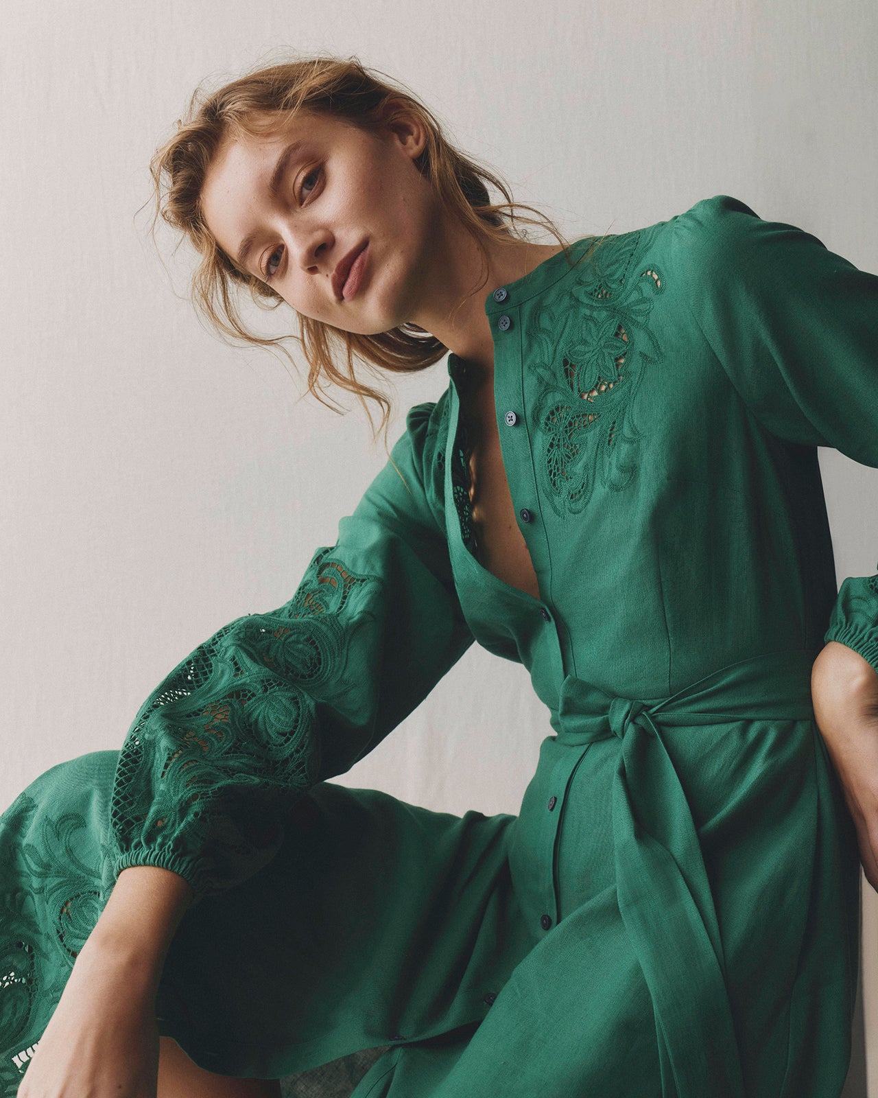 Woman wearing a green dress with intricate detailing against a plain background