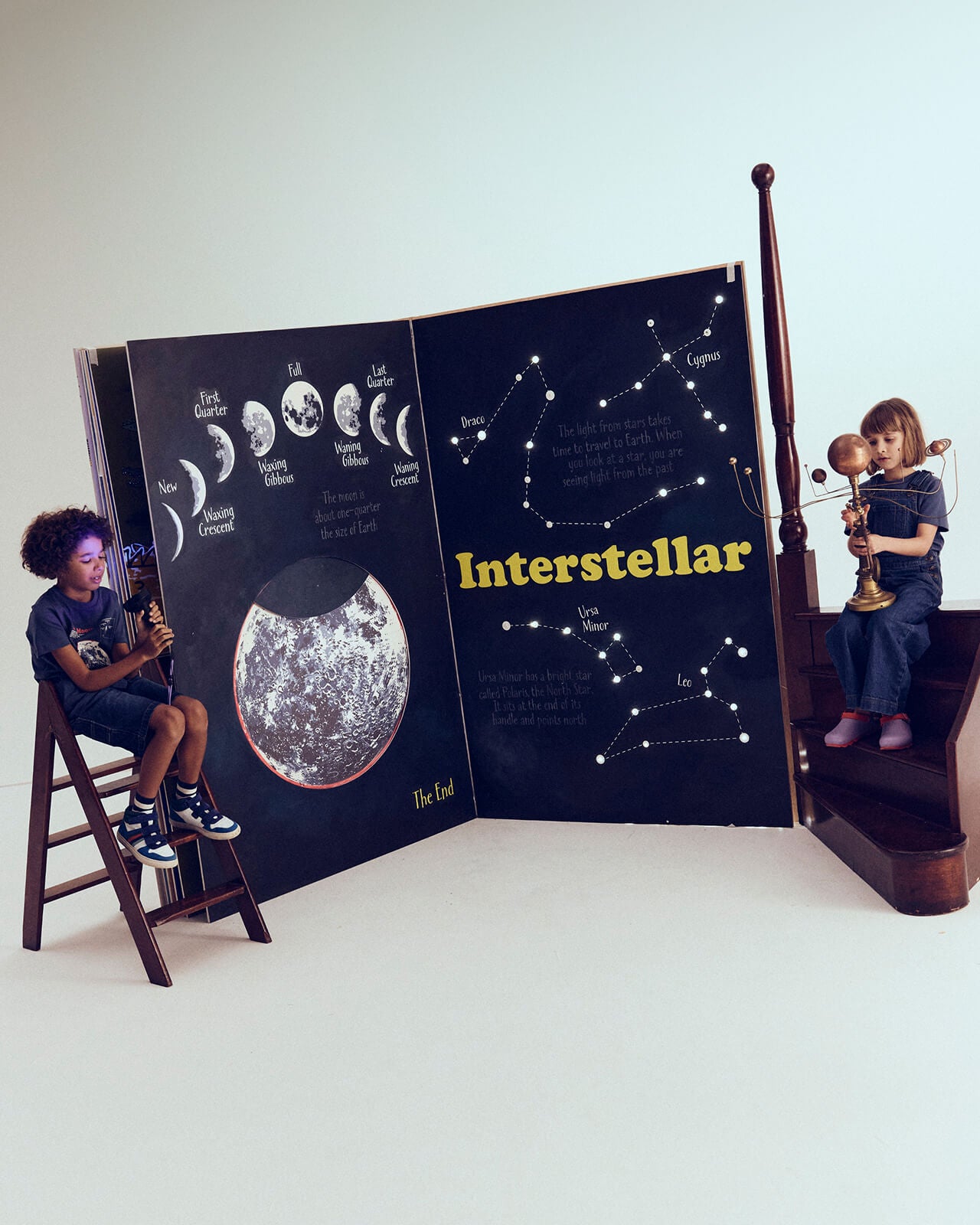 Children playing with a large 'Interstellar' book open to a space-themed page.