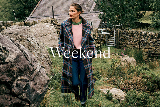 Woman in a plaid coat standing in a rustic outdoor setting with the word 'Weekend' displayed.