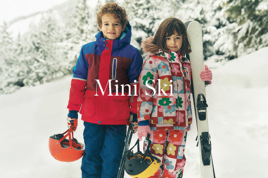 Two children in colourful ski outfits standing in the snow with ski equipment, featuring the brand 'Mini SKI'.