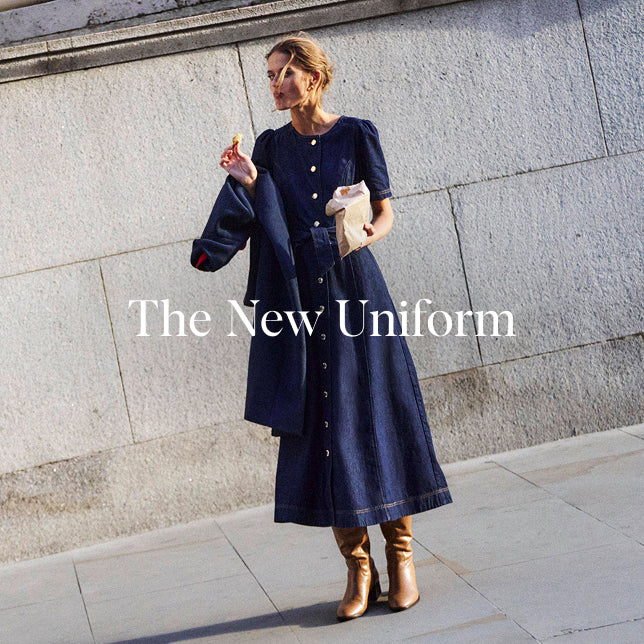 Woman wearing a navy dress with 'The New Uniform' text overlay against a stone wall.
