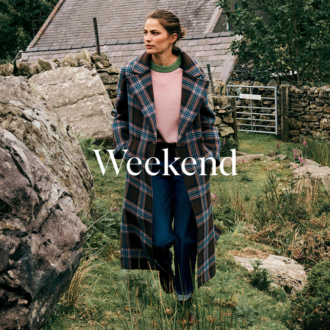 Woman in a plaid coat standing in a rustic outdoor setting with the word 'Weekend' displayed.