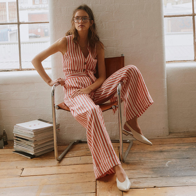 Woman in a red and white striped jumpsuit sitting on a chair in a room with large windows.