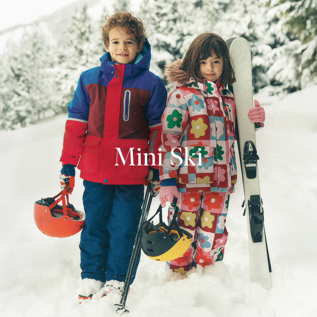 Two children in colourful ski outfits standing in the snow with ski equipment, featuring the brand 'Mini SKI'.