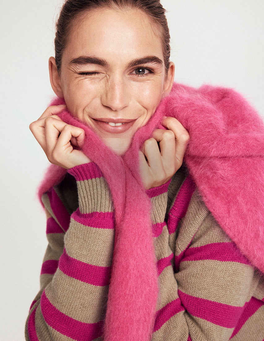 Person wearing a pink and brown striped sweater with a pink fur collar against a white background