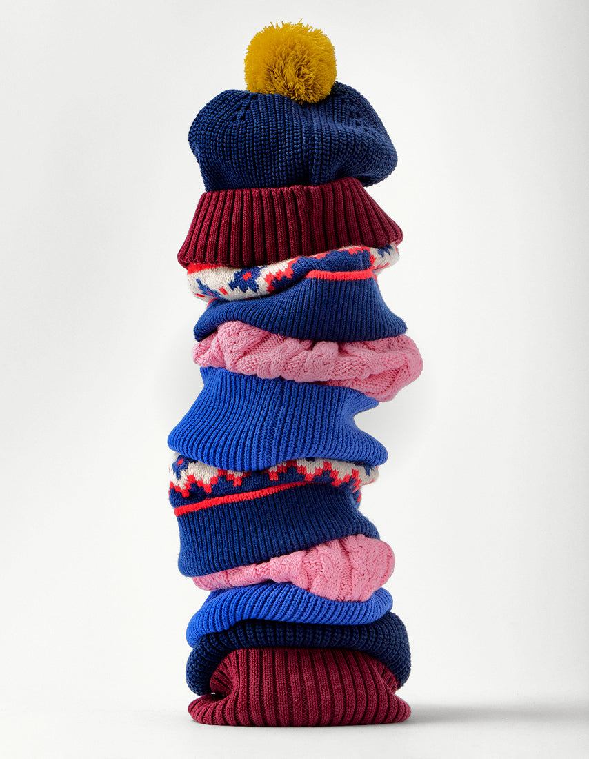 Stack of colorful knitted sweaters and hats on a white background