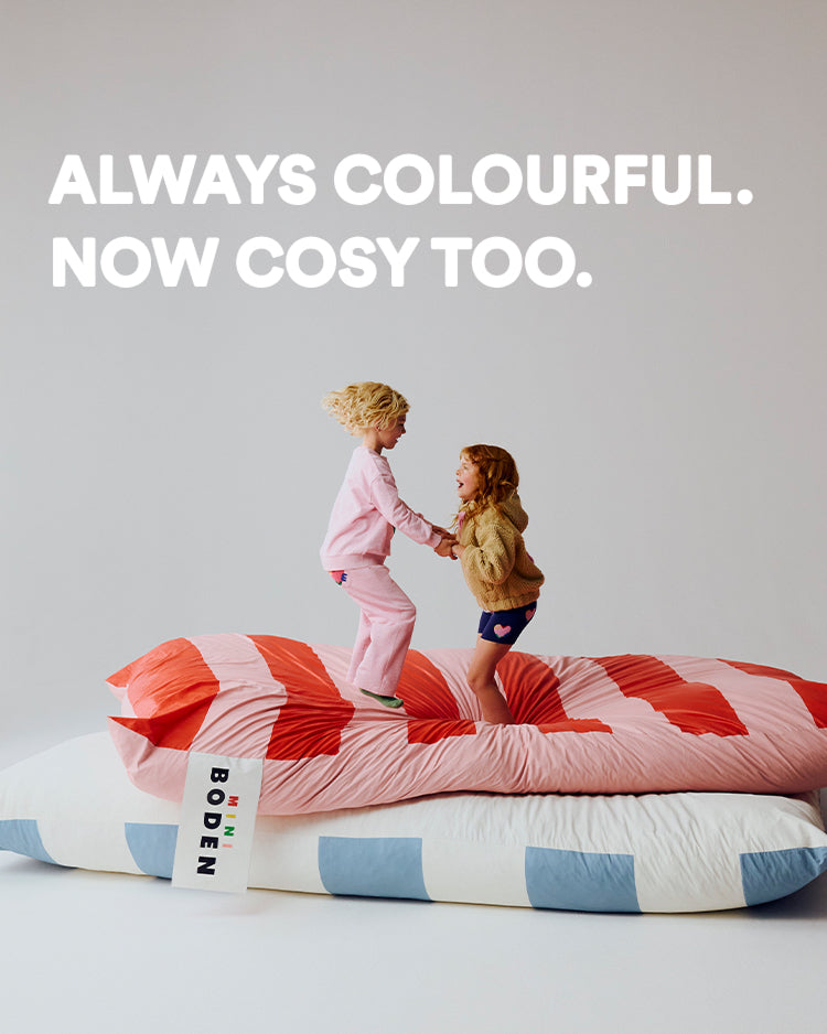 Two children on a bed with a colourful quilt, text 'Always Colourful. Now Cosy Too.'