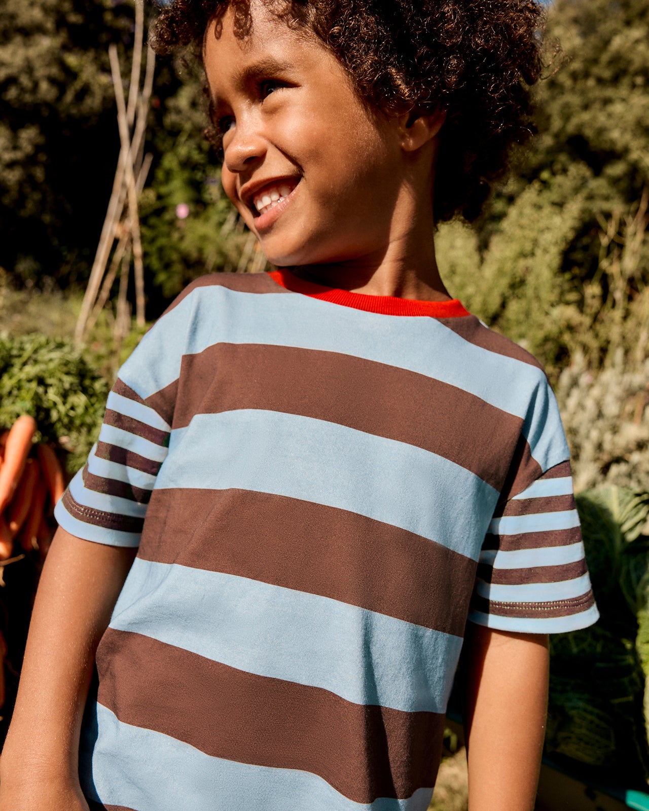 Child wearing a striped shirt outdoors with greenery in the background