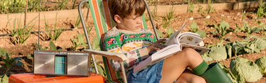 Child sitting in a garden reading a book with a radio on a chair