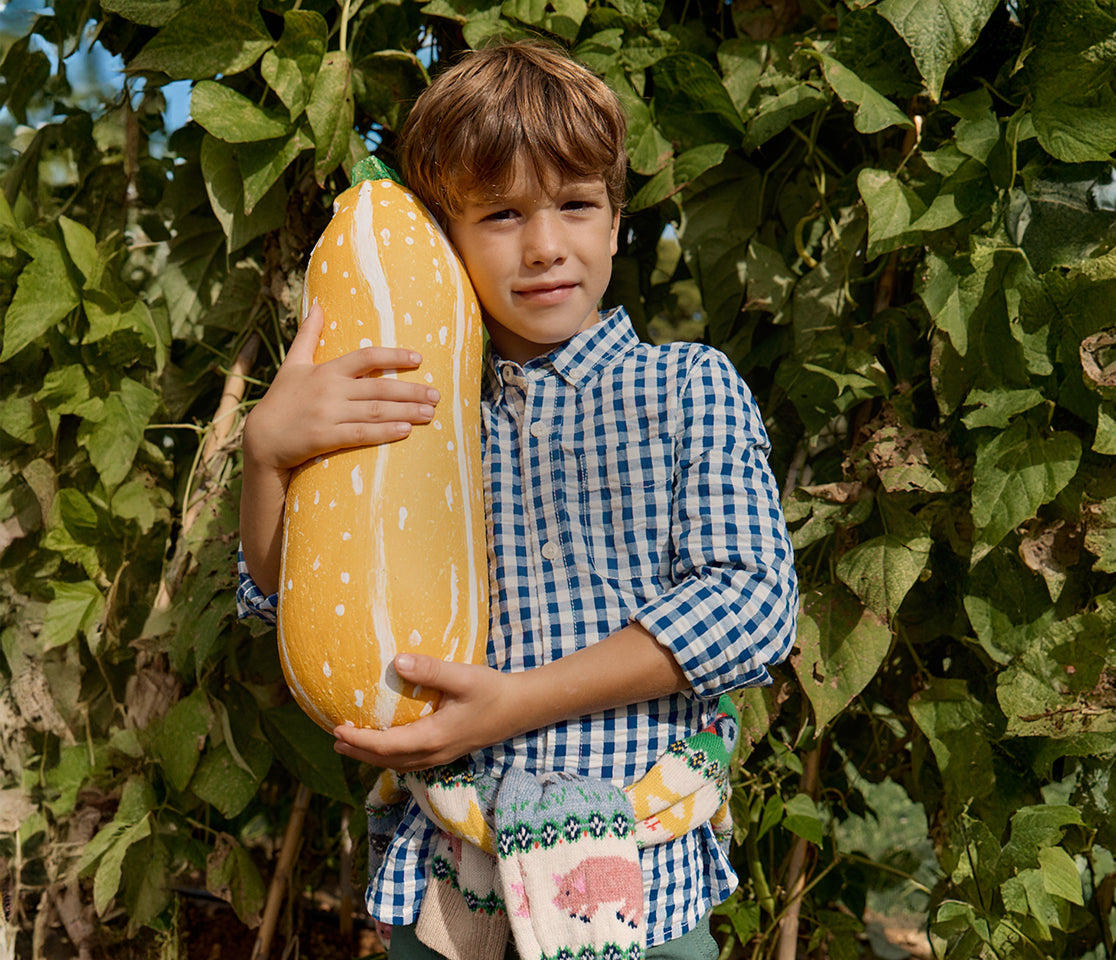 Child holding a large toy hot dog outdoors among green leaves