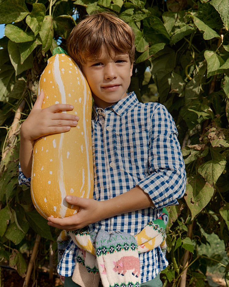 Child holding a large yellow plush toy in front of green foliage