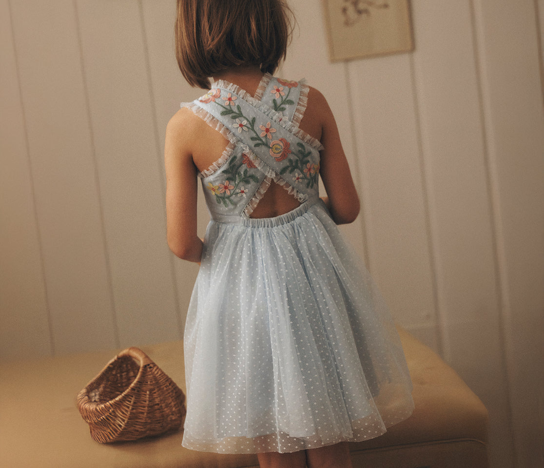 Child wearing a floral dress with an open back, standing in a softly lit room.