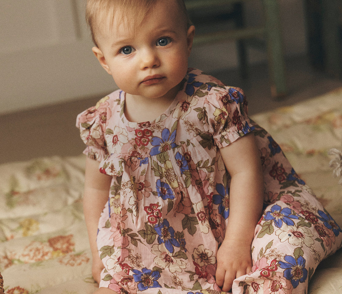 Baby wearing a floral dress sitting on a couch.