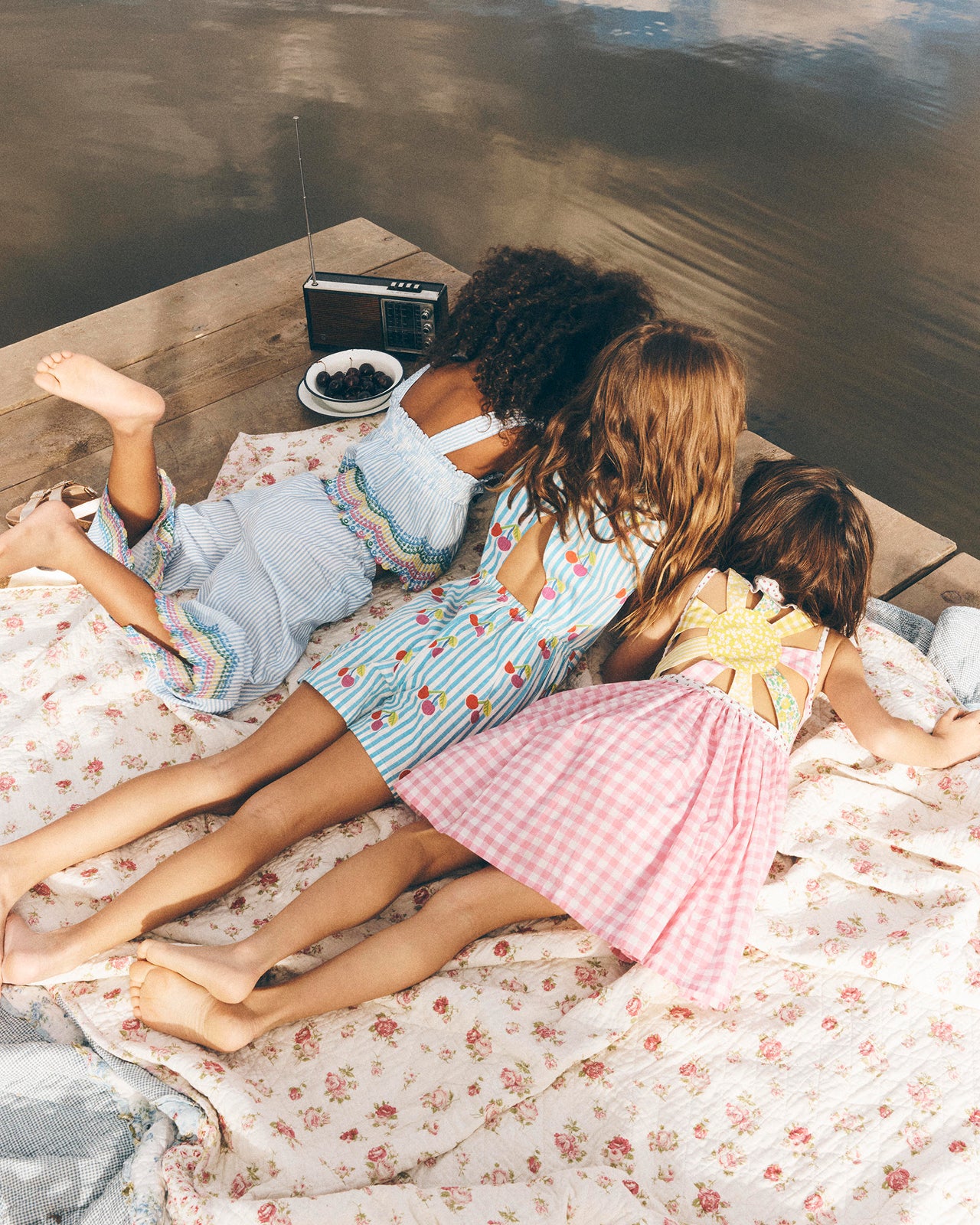 Three children in pajamas lying on a bed with a floral blanket, looking at a radio.