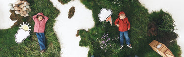 A whimsical overhead scene of two children lying on grassy islands, each wearing a raincoat and jeans, surrounded by cartoon-style cloud cutouts, a small wooden boat, and natural elements on a white background.