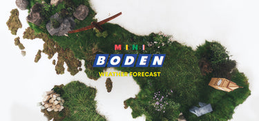 A top-down view of a miniature diorama representing the continent of Europe, covered in green grass and moss with small rocks, trees, and a tiny boat. The text 'MINI BODEN WEATHER FORECAST' is overlaid in the center on a white background.