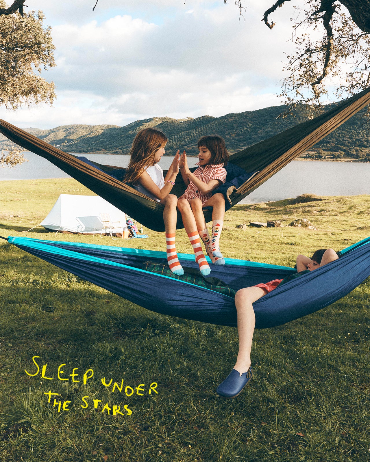 Two children sitting in a hammock with a scenic background and text 'Sleep under the stars'.
