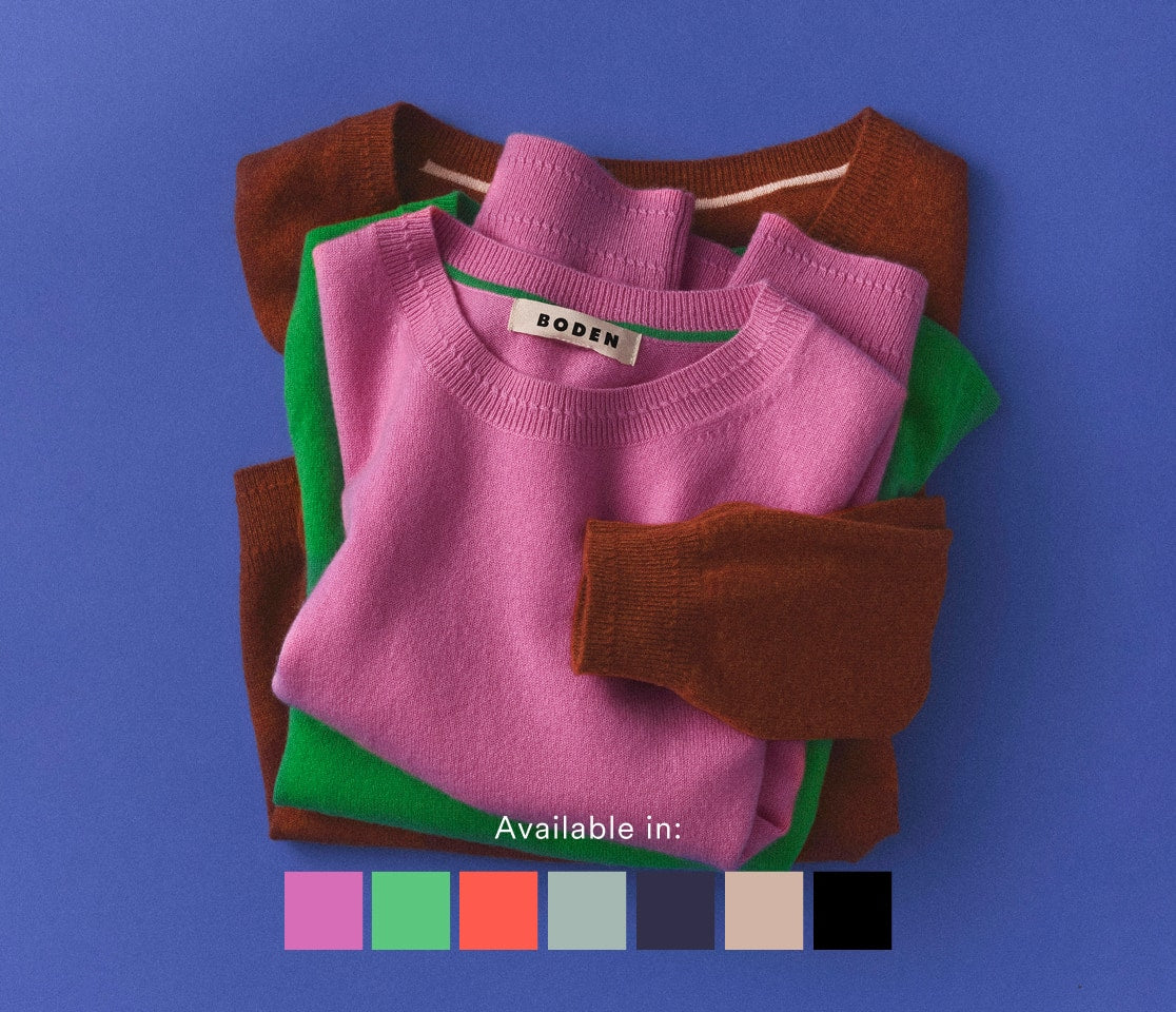 Stack of colorful sweaters on a wooden hanger against a blue background, with BODEN branding.