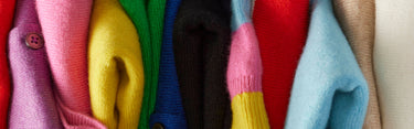 Stack of colorful sweaters in various colors including pink, yellow, green, black, red, blue, and beige.