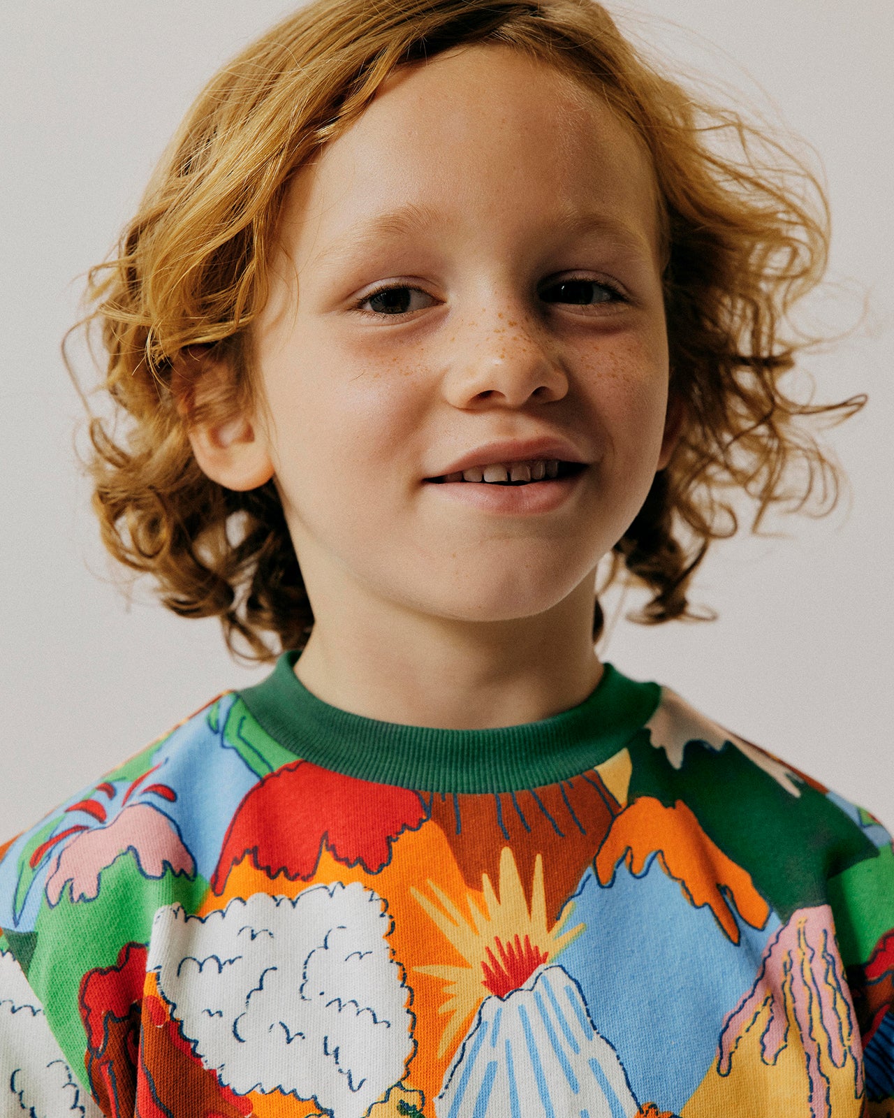 Child wearing a colourful sweater with abstract designs on a plain background