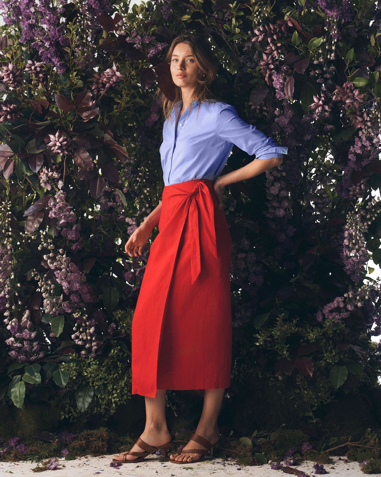 Woman in a blue shirt and red skirt standing against a floral background