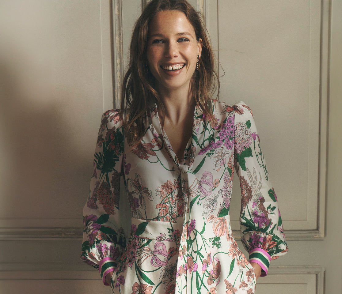 Woman wearing a floral blouse standing against a neutral wall.