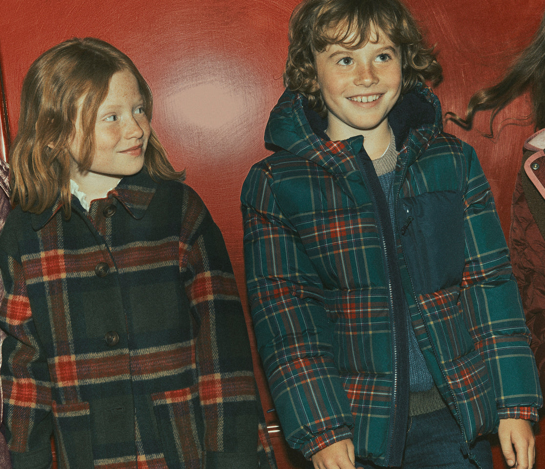 Children in Tartan jackets standing against a red wall