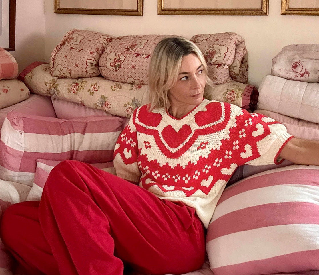 Woman wearing a red and white patterned sweater sitting on a floral-patterned couch.