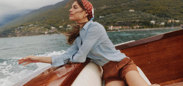 Woman sitting in a wooden boat on a body of water with mountains in the background