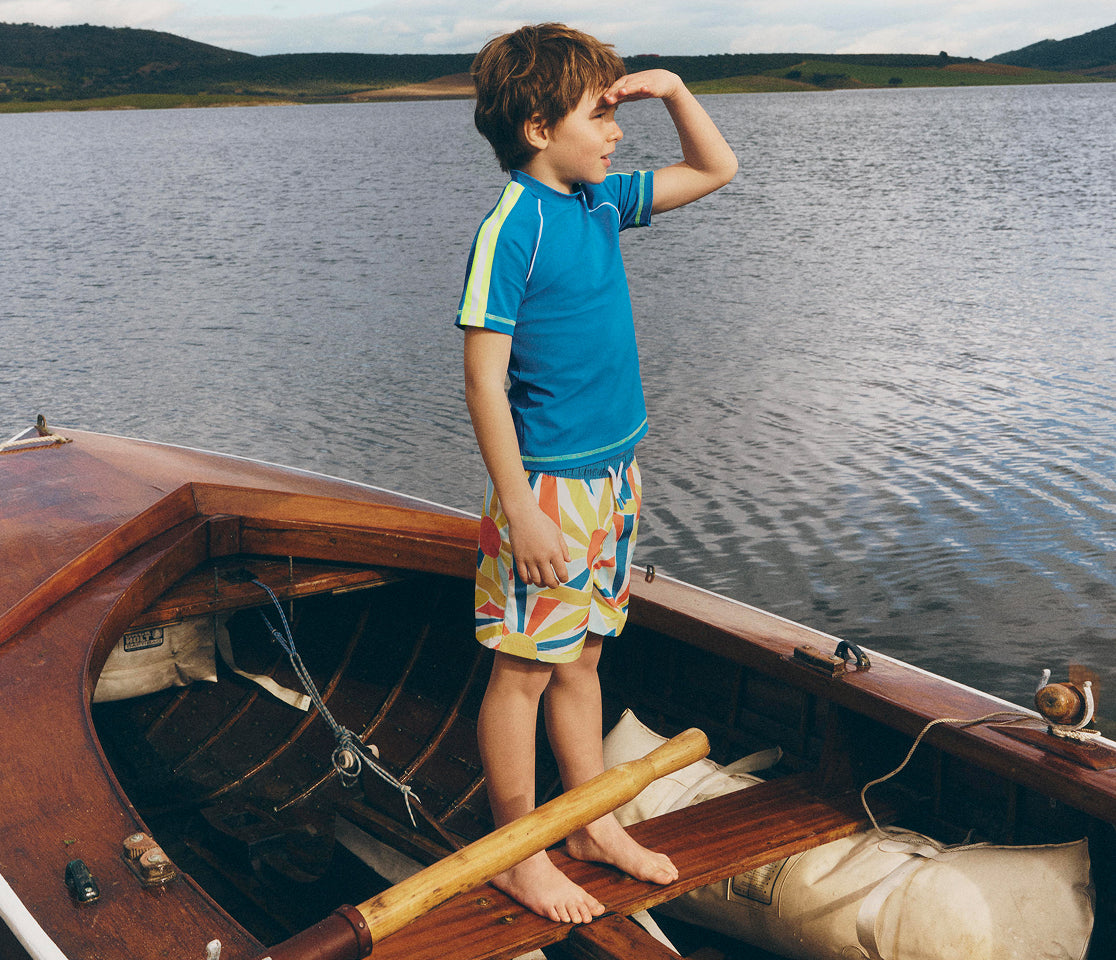 Child standing on a wooden boat by a lake