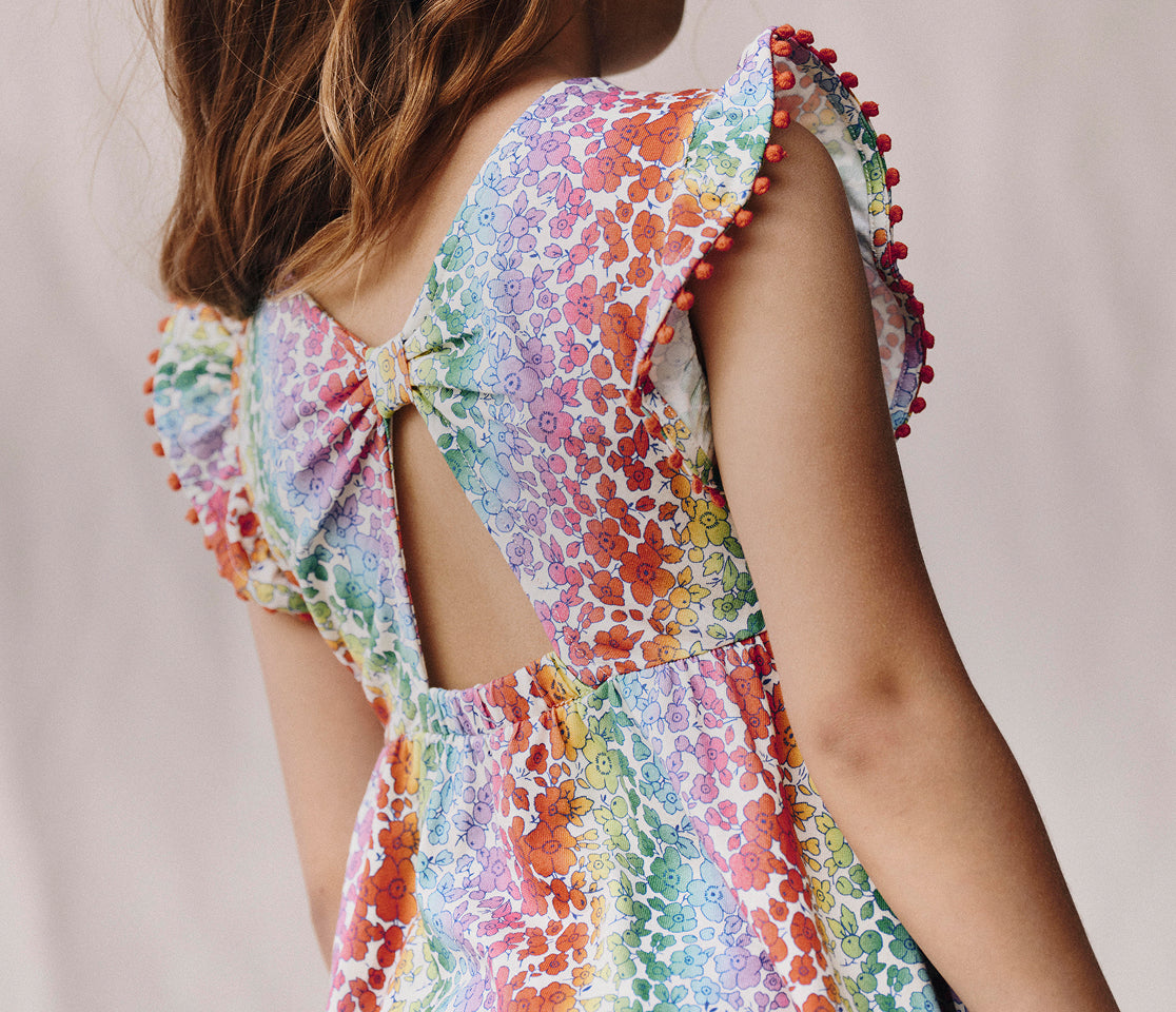 Colorful floral dress with open back and pom-pom details on a plain background