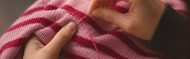 Person sewing red thread into a pink fabric with a blurred background