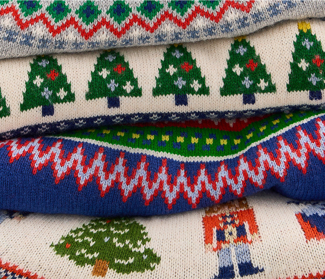 Stack of knitted sweaters with Christmas tree and Santa Claus patterns.