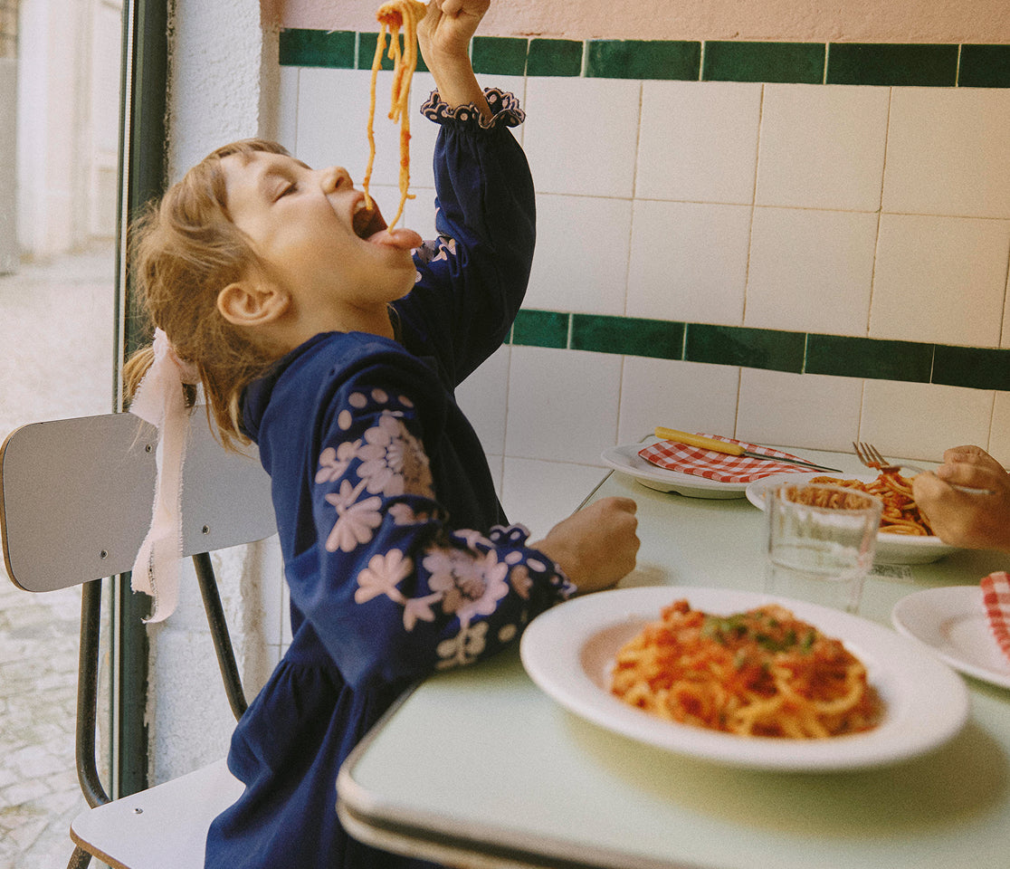 Child eating spaghetti at a table with a tiled wall background