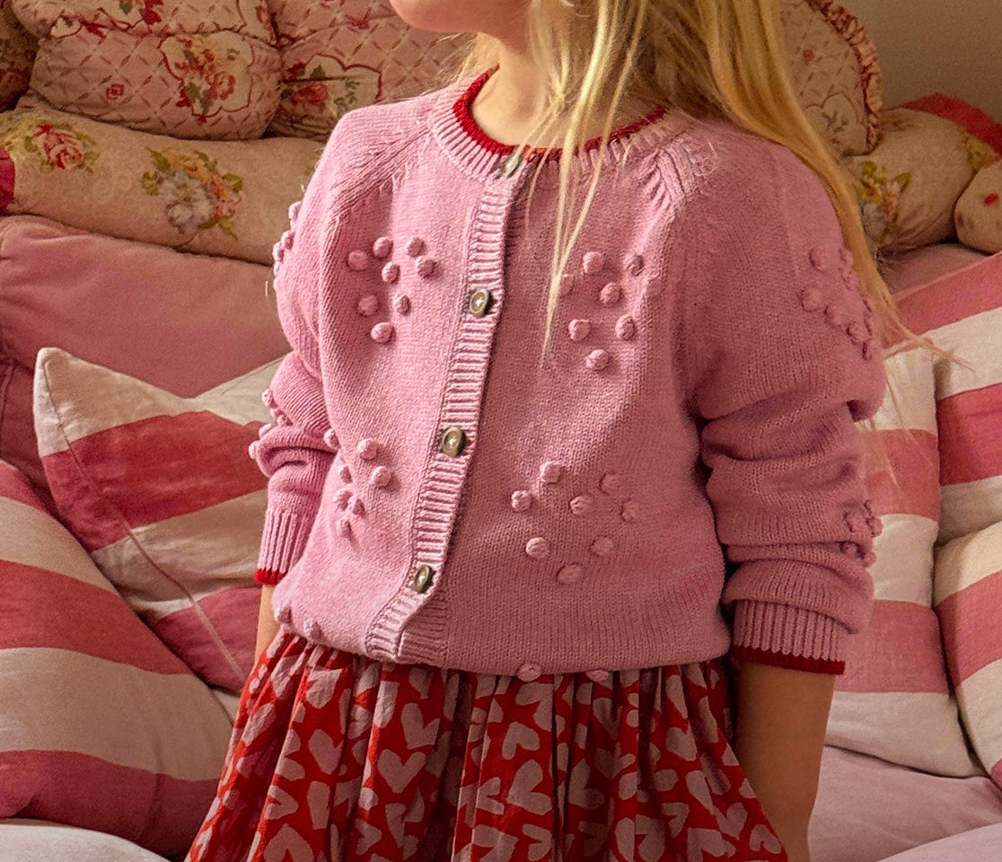 Child wearing a pink cardigan with button details in a cozy indoor setting.