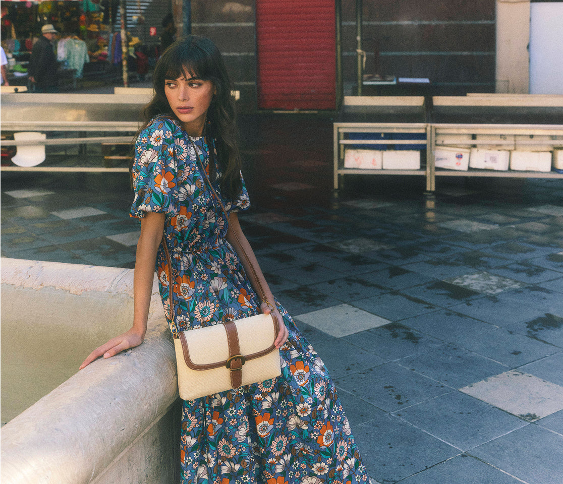 Woman in a floral dress holding a beige handbag in an urban setting