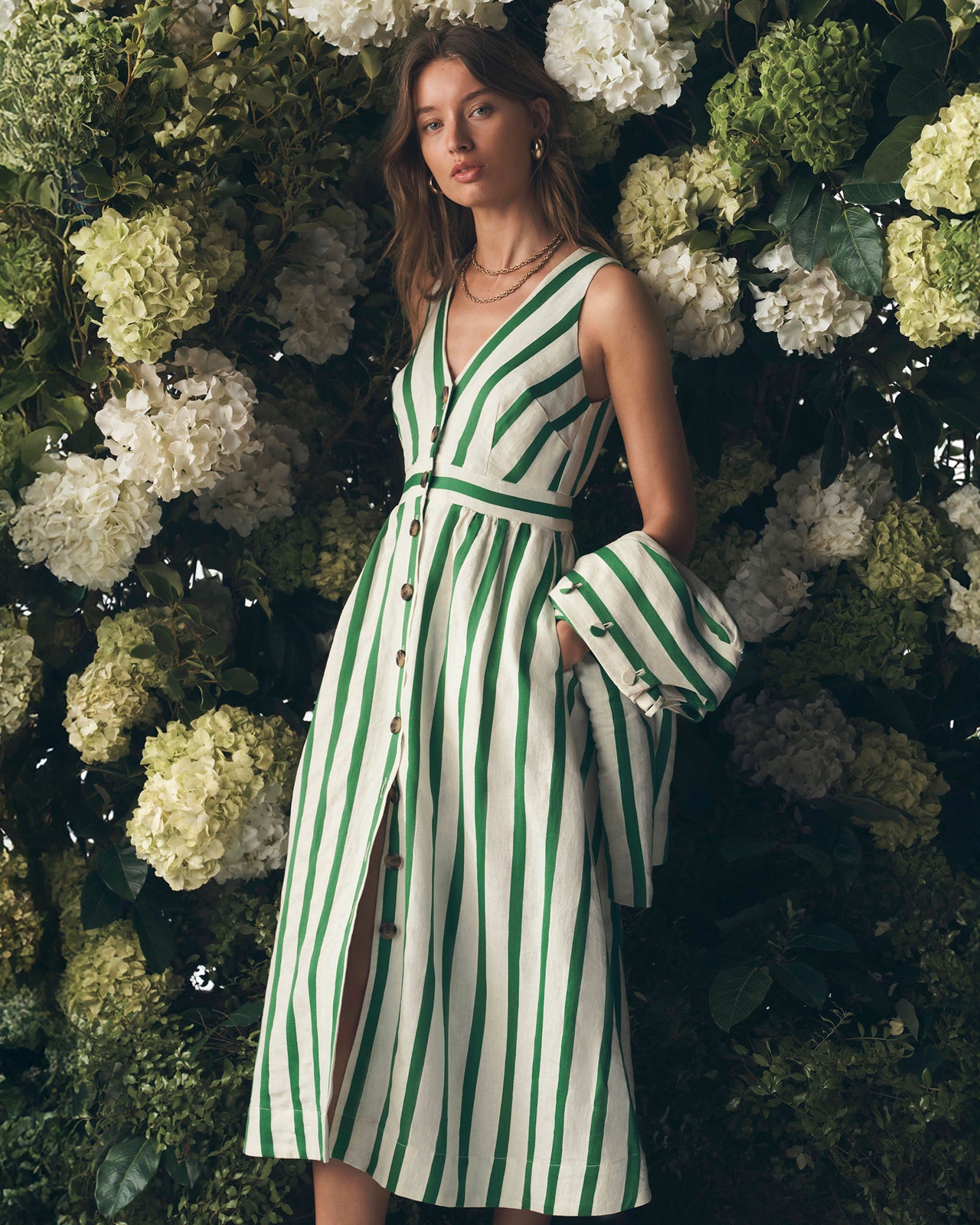 Woman in a green and white striped dress standing against a floral background