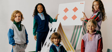 Five children in colourful clothing standing around a large playing card with geometric shapes on a plain background.