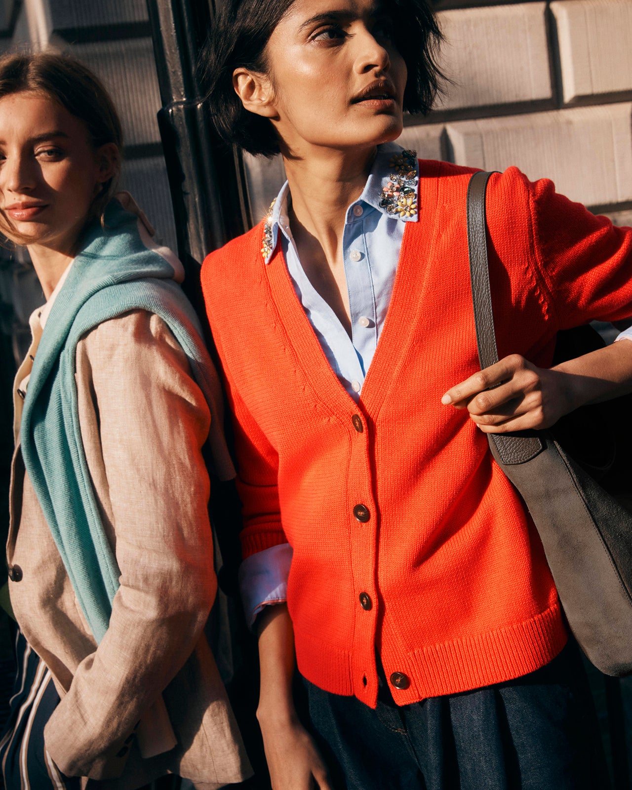 Two women standing close to each other, one wearing a red cardigan and the other in a beige jacket.