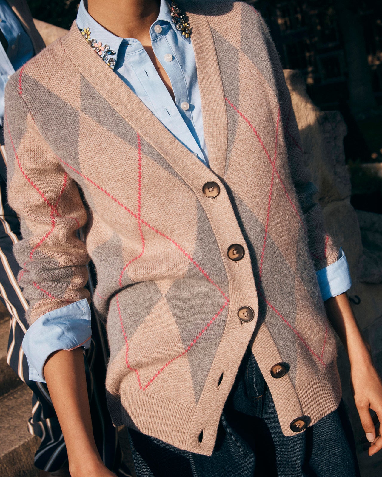 Person wearing a beige cardigan with a patterned design, button details, and a light blue shirt underneath.