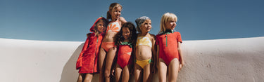 Five children in colorful swimsuits standing against a clear blue sky.