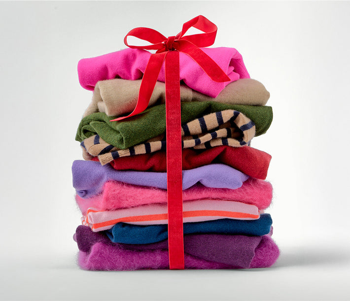 Stack of colorful folded clothes tied with a red ribbon on a light gray background