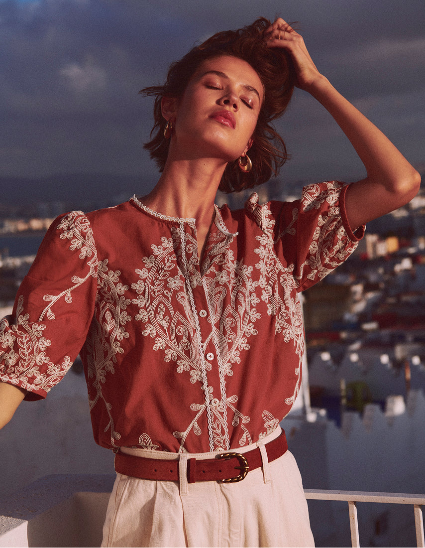Woman wearing a red embroidered blouse with a scenic background