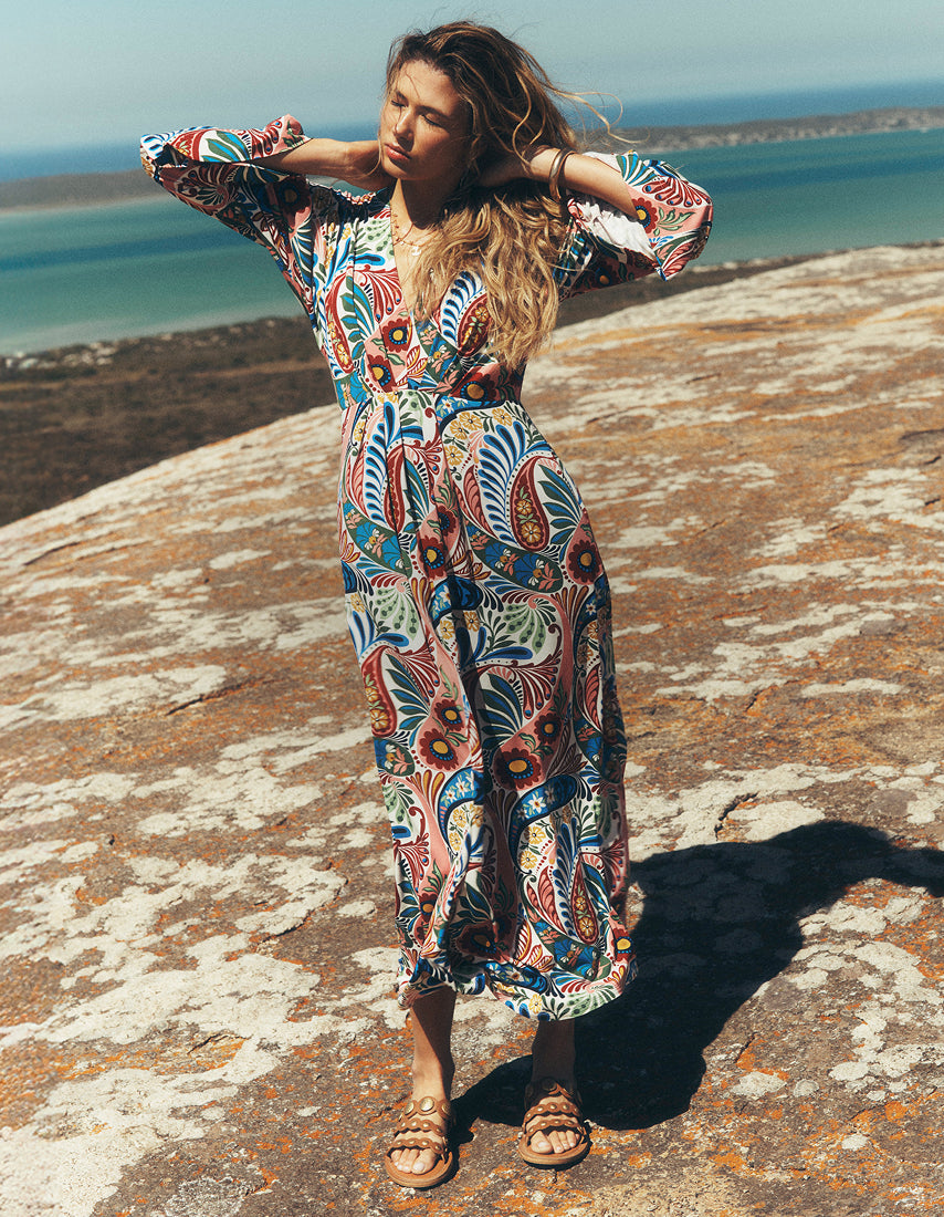 Woman in a colorful patterned dress standing on a rocky outcrop with ocean view